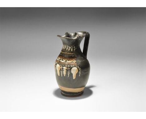 5th-3rd century BC. A blackware ceramic oinochoe with tiered foot, broad pouring lip and strap handle to the rear; band of ov