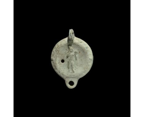 2nd century AD. A terracotta discoid lamp with pierced lug handle to the rear, D-shaped nozzle; ring-and-dot motifs to the sh