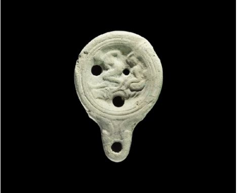 1st century AD. A discoid terracotta lamp with short nozzle and volute scrolls, broad discus with three holes, scene of two l