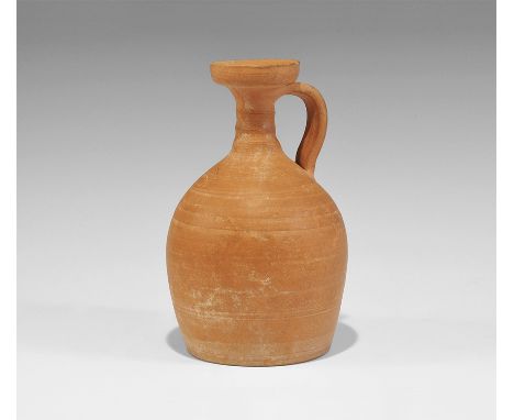 1st-3rd century AD. A redware ceramic vessel with bulbous body, ribbed neck, broad mouth with vertical rim, facetted strap ha
