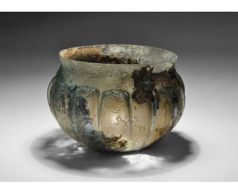 3rd-4th century AD. A pale blue glass bowl with iridescent surface, flat bottom, pinched vertical ribbing, slightly everted r