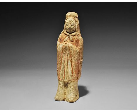 Northern Qi Dynasty, 550-577 AD. A hollow-cast ceramic figurine of a standard bearer in hood and cape, hands drawn up the che