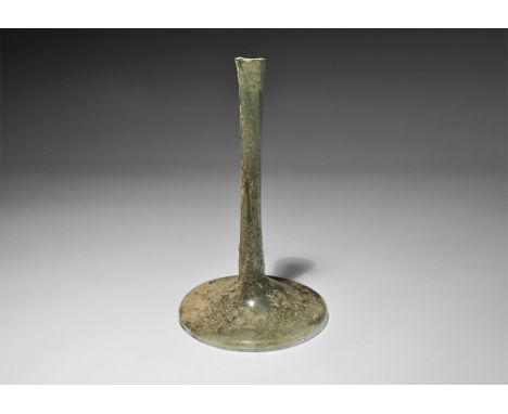 1st-3rd century AD. A pale green glass vessel with shallow flared base concave to the underside, narrow stem neck. Cf. Whiteh