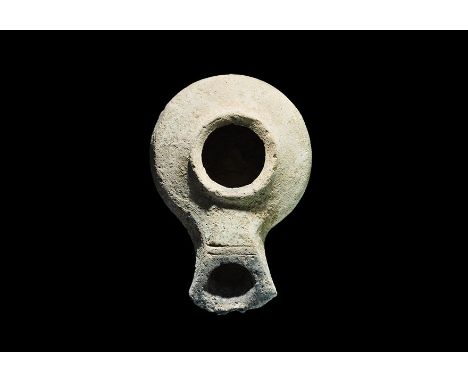1st century BC-1st century AD. A squat terracotta oil lamp with broad discus, short pelta-shaped nozzle with transverse strok