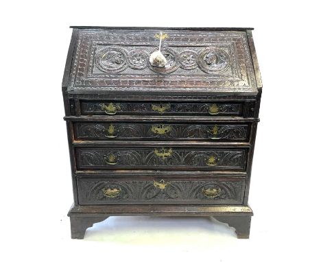 A George III carved oak bureau, the fall front carved with three portraits enclosing a fitted interior, above four long gradu