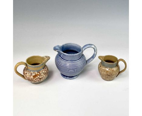 A engine turned jug, circa 1820, overglazed in blue, height 8cm, together with two small coggled slip glazed jugs. (3)