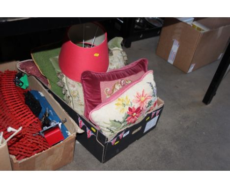 A box of various cushions and two red lamp shades 
