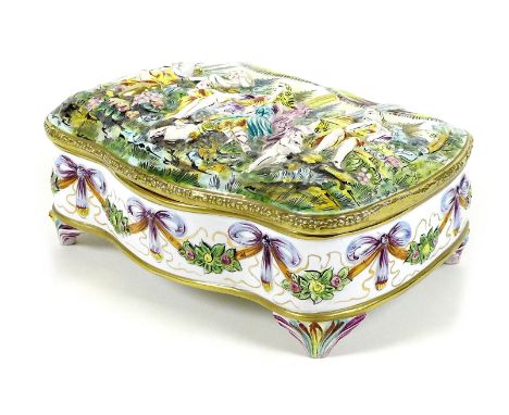 A Capodimonte ceramic box, of shaped outline, the hinged cover moulded in relief with a Bacchanalian scene, on four feet, 31 