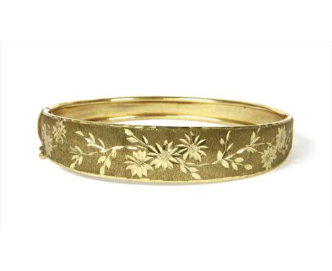 A 9ct gold hinged bangle, the tapering upper half with bright cut floral engraving to a textured ground, to plain lower half,