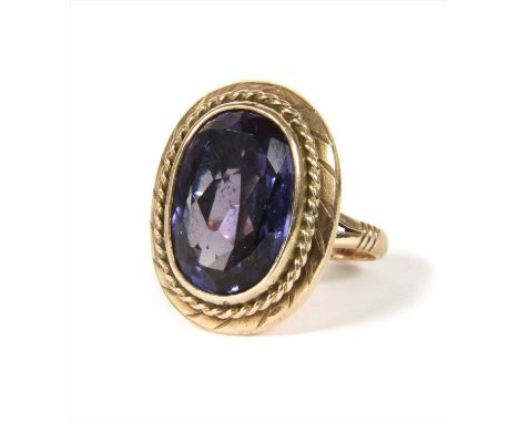 A gold synthetic colour change sapphire ring, with an oval mixed cut synthetic colour change sapphire, rub set to twisted wir