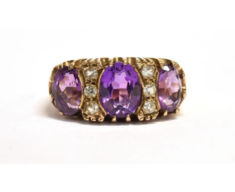 AN AMETHYST THREE STONE 9CT GOLD RING Three oval cut amethyst, the centre stone approx. 8mm x 6 mm with small white stone bet