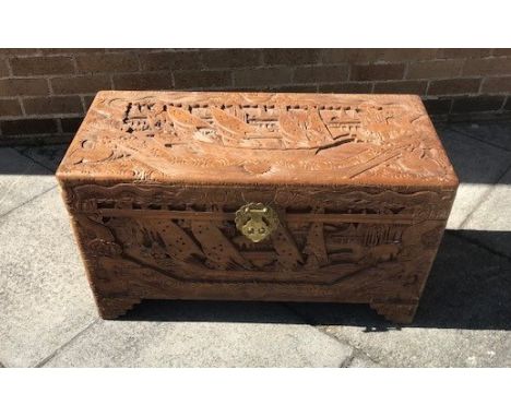 AN ORIENTAL CAMPHOR WOOD TRUNK, with carved decoration to the front and sides depicting boats and figures, 48cm x 88cm x 42cm