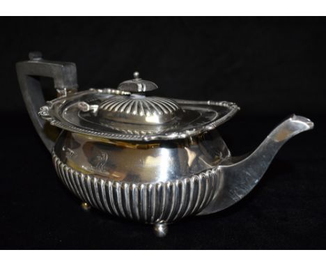 A SILVER CUSHION SHAPED TEAPOT  With half fluted decoration and scroll and grooved border on four ball feet, engraved crest, 