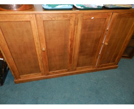 An early 20th century light oak low four door cabinet, the doors opening to reveal three fixed shelves.