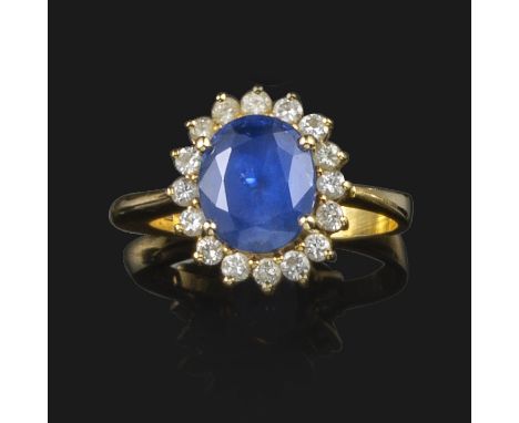 A sapphire and diamond cluster ring, the oval-shaped sapphire is set within a surround of diamonds in yellow gold, size N