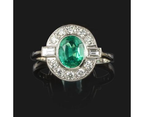 An emerald and diamond cluster ring, the oval-shaped emerald is set within a surround of round brilliant-cut diamonds, with a