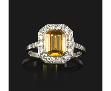 A yellow sapphire and diamond cluster ring, the emerald-cut yellow sapphire set within a surround of round brilliant-cut diam