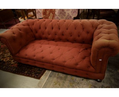 A LATE VICTORIAN CHESTERFIELD SETTEE. Button back, seat and sides, raised on frontturned legs. Covered in iron-red fabric, 76