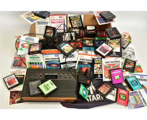 A BOX CONTAINING AN ATARI 2600 CONSOLE, GAMES, MANUALS AND CONTROLLERS, games include Donkey Kong, Defender, Pac-Man, Breakou