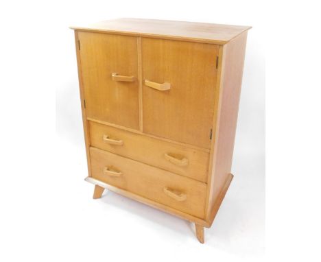 A vintage mid century light oak and teak linen press, two doors opening to reveal a single shelf above two long drawers, rais
