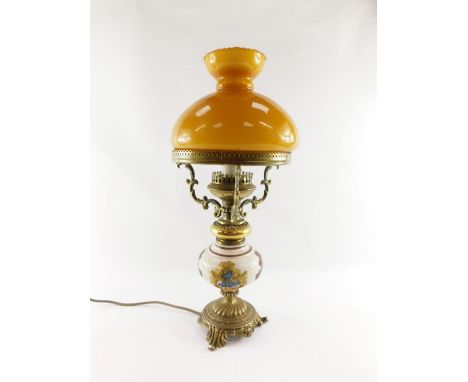 A 20thC oil lamp style electric table lamp, with orange glass shade on a brass three prong support, with glazed and floral pr