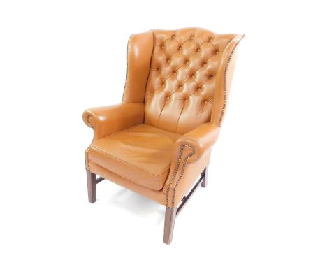 A Georgian style mahogany wing armchair, upholstered in button back tan leather, with loose cushion seat, raised on tapering 