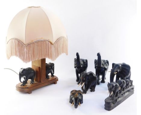 A group of ebony carved elephant ornaments, and a table lamp with two elephants to the base, frilled peach shade, 50cm high. 
