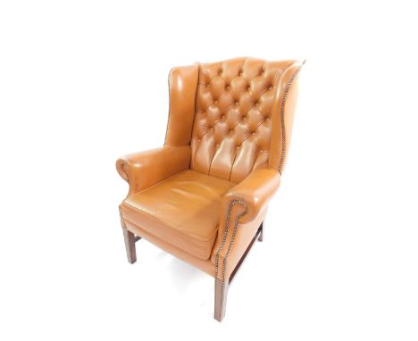 A Georgian style mahogany wing armchair, upholstered in button back tan leather, with loose cushion seat, raised on tapering 