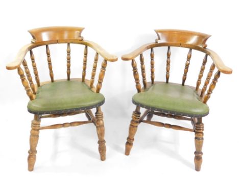 A pair of Victorian oak smoker's bow chairs, with later green button leatherette seats, raised on turned legs.