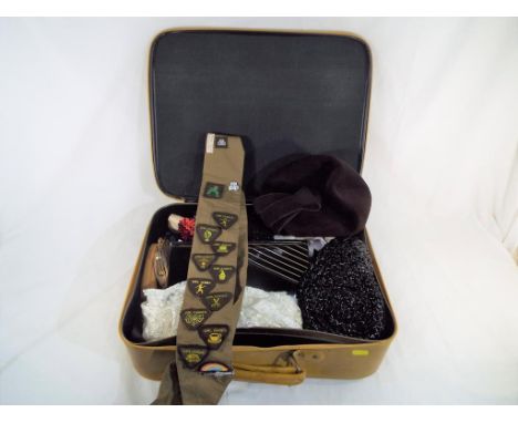 A vintage suitcase containing a quantity of clothing to include hats, gloves, purses and a Girl Guide sash with badges