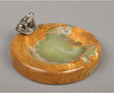 A polished onyx trinket dish surmounted with a white metal figure of a frog. Diameter of dish 12cm.  
