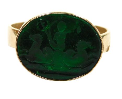 A green glass intaglio ring, of oval form, intaglio decorated with Poseiden being drawn by two hippocampi, in a yellow metal 