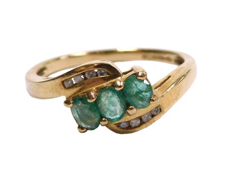 A 9ct gold and emerald three stone ring, in a crossover design, the shoulders each set with four tiny diamonds, size O 1/2, 2