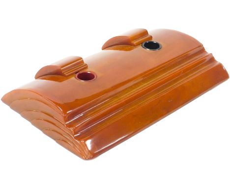 An Art Deco orange Bakelite desk stand, with two inkwells, and pen recesses, 29cm wide.