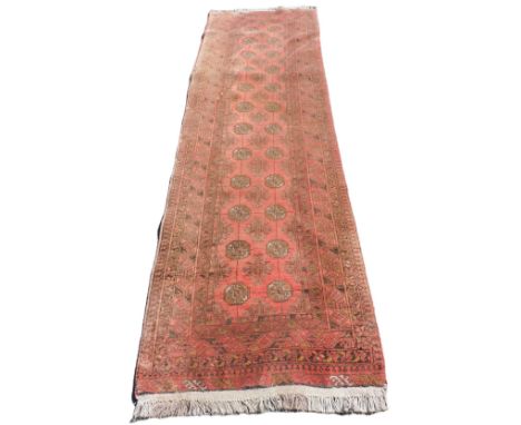 A Bokhara red ground runner, the central field with twenty four medallions and eleven floral motifs, within borders or repeat