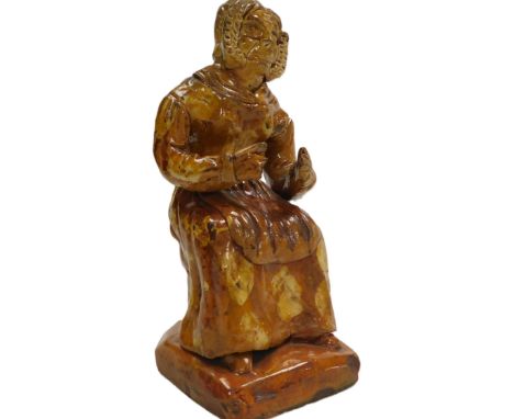 A mid 19thC Welsh Pill Pottery red slipware pottery figure of a lady, modelled seated wearing a dress, apron and bonnet, 19cm