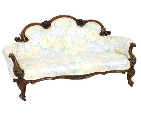 A Victorian walnut show frame sofa, carved with scrolls and flowers, with a padded back, armrest and seat, upholstered in flo