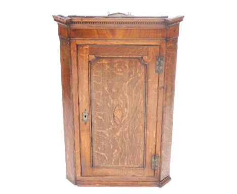 A George III oak and mahogany hanging corner cupboard, with an outswept pediment with dentil moulding, over a panelled door w