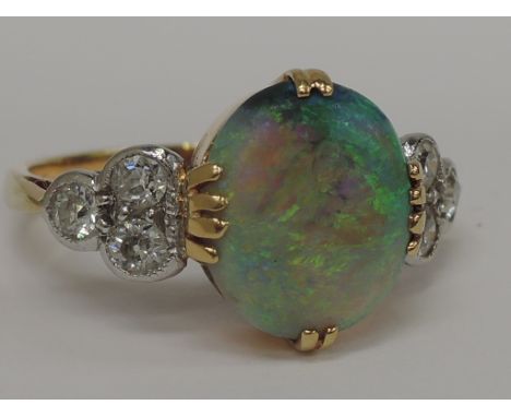 A ladies dress ring having a large opal in a claw setting with trio of diamonds to each shoulder on an 18ct gold loop