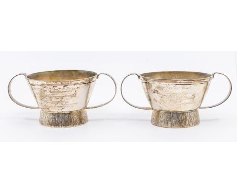 A pair of Queen Elizabeth II modernist silver condiment pots, both twin handled and with textured designs to foot circular fo