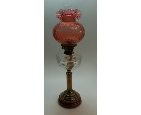 A glass oil lamp base with a cranberry shade
