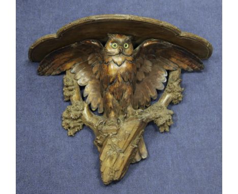 A late 19th / early 20th century Black Forest carved wall bracket, modelled as an owl, with glass eyes, perched on a rock wit