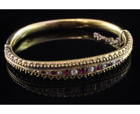 A late Victorian 15ct gold, ruby and diamond set hinged bracelet, set with fifteen graduated stones with a ropetwist and bead