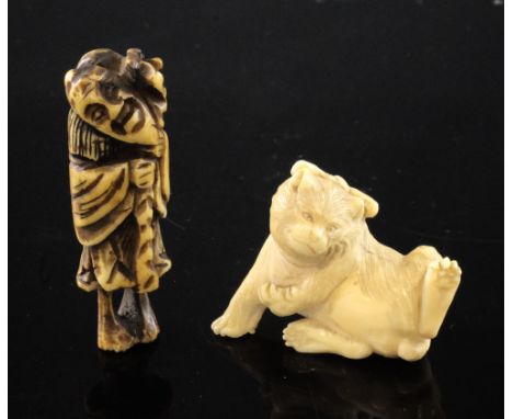 A Japanese ivory figure of a cat and a stag horn netsuke, the cat with a tied bow to its head, playfully leaning to one side,