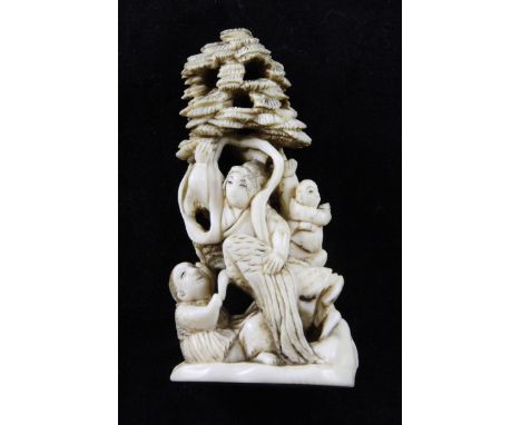 A Japanese ivory okimono netsuke, early 20th century, carved with a female immortal and other figures beneath a pine tree, 7.