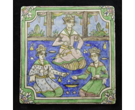A Persian Qajar dynasty moulded polychrome pottery tile, decorated under the glaze with an interior scene of three seated fig