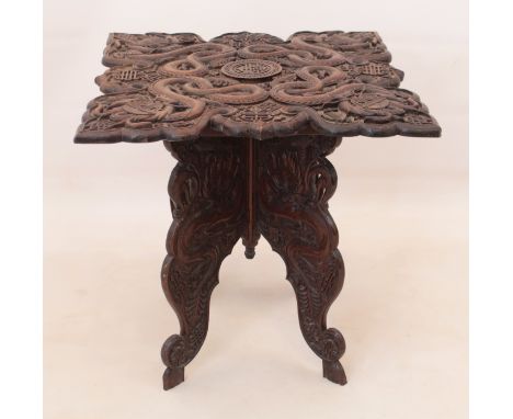 A Chinese carved hardwood folding occasional table - early 20th century, the shaped top carved with four long-bodied dragons 