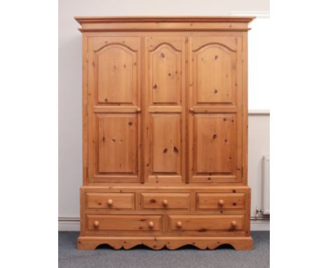 A waxed pine triple wardrobe - with a moulded cornice over three two-panel doors, enclosing a brass hanging rail, on a base w