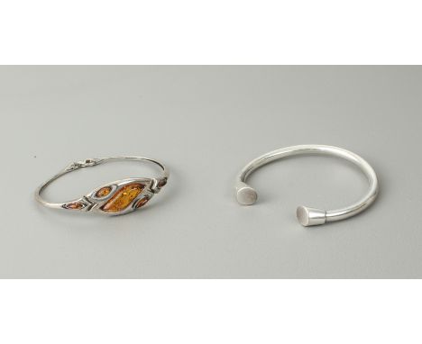 Two sterling silver bangles - one hinged with a central lobster claw clasp, set with polished amber; the other of torc-style.