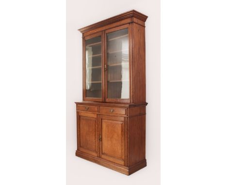 A late-Victorian oak cupboard-bookcase - the flared, moulded cornice over four adjustable shelves behind two glazed doors, th
